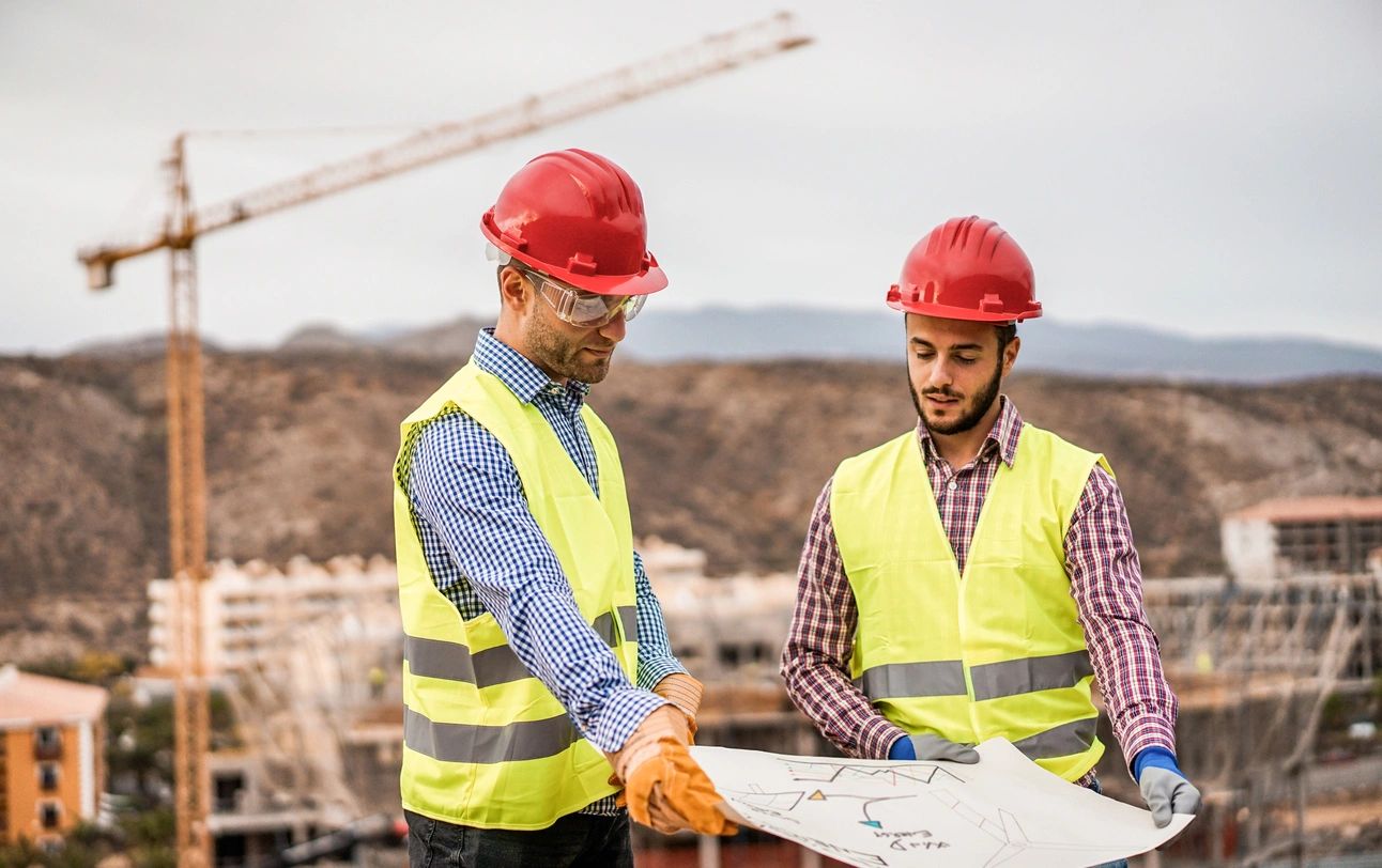 Two men in yellow vests and hard hats holding a map.